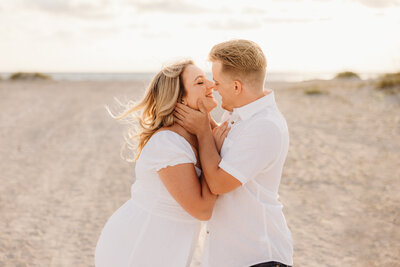 Man getting ready to kiss woman while her hair blows in the wind on the beach while taking engagement photos in Tampa.