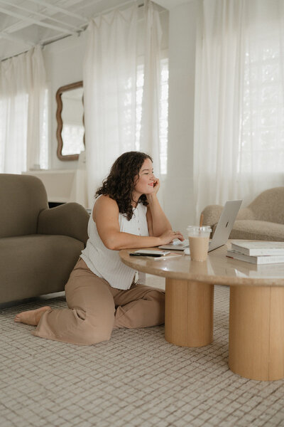 Morgan carrying a laptop and coffee cup by a table