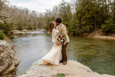 Groom-kisses-bride- on temple- in front of elopement ceremony arch in  Virginia forest