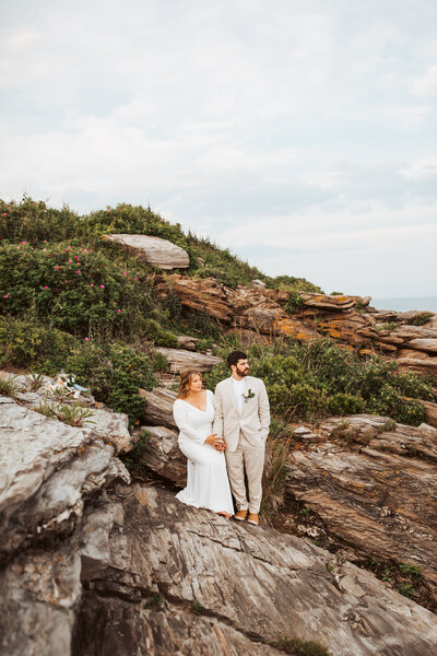 Engaged couple standing together on rocky coastal cliffs during their Maine engagement session.