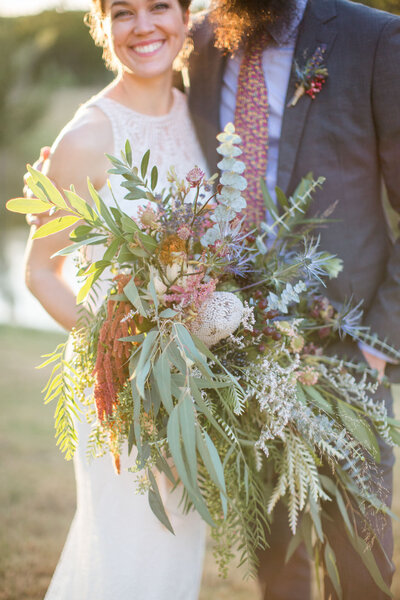 Close up photo of a wedding bouquet being held by the bride with her groom beside her