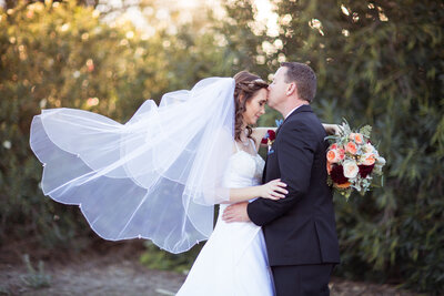 Groom kisses his Bride's forehead as her veil flies in the air