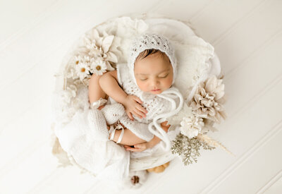 Newborn baby wearing a simple floral headband, asleep on a textured blanket, photographed in an elegant fine-art style.