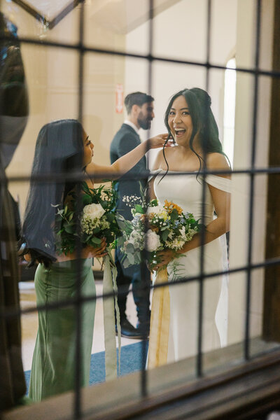 Photo taken through a window of bridesmaid fixing bride's hair