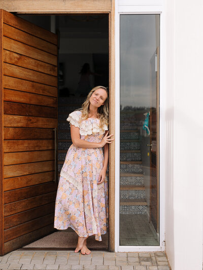 A lady stands at the doorway , looking at the camera in a creative lifestyle pose