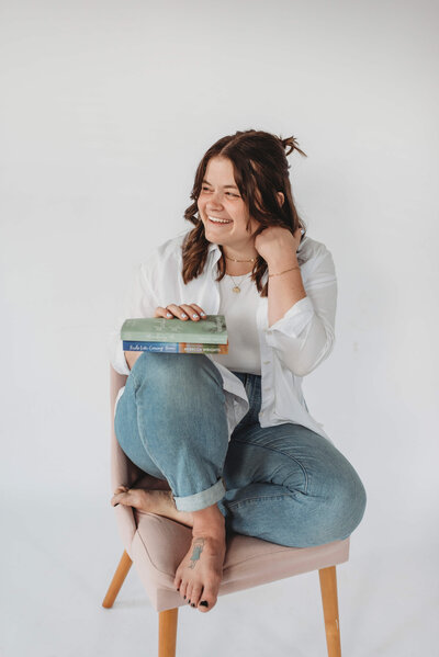 Woman with brown hair kneeling on  stool holding book