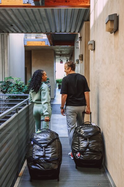 Couple walk down a hotel hallway pulling their luggage