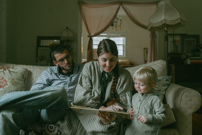 parents sitting on couch reading to their son during family photos captured by NYC family photographer Elsie Goodman