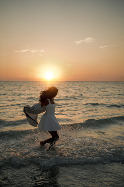 master's graduate running with grad gown along the beach in shallow water