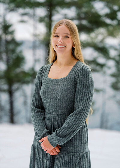 Young woman smiling during a winter portrait session, photographed outdoors in a snowy forest by Joseph Mayden using natural light and lifestyle-inspired posing.
