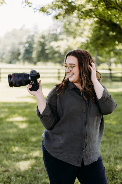 photographer posing with her camera looking off to the side and playing with her hair