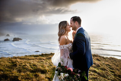 A bride and groom laughing together on a cliff overlooking the Oregon coast, captured by an Oregon elopement photographer