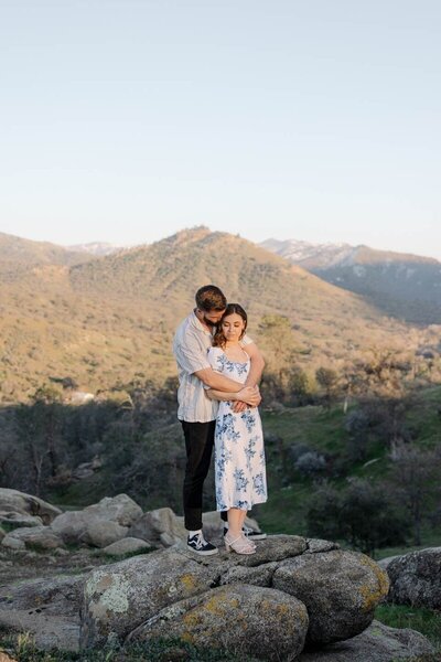 couple embraced standing on rocks with mountain view in background taken by minneapolis engagement photographer tom thornton 