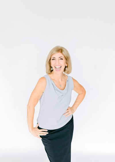 Lora Ulrich in a grey sleeveless top holding a mug, smiling at the camera.