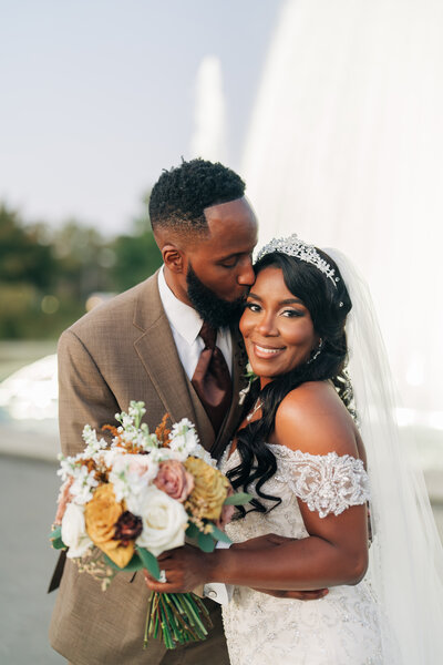 A groom kissing his bride in front of a fountain on their wedding day