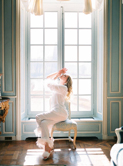 Bride getting ready for her Paris wedding in Chateau de Villette by the window with cinematic sunlight