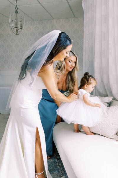 Bride and bridesmaid helping pin flower girl's dress