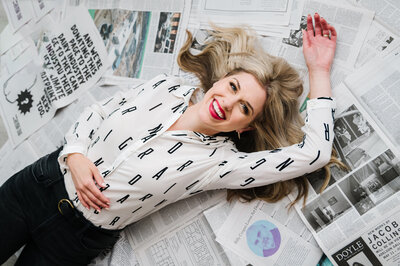 Sarah Klongerbo smiling and laying on the floor on top of a bunch of newspaper pages