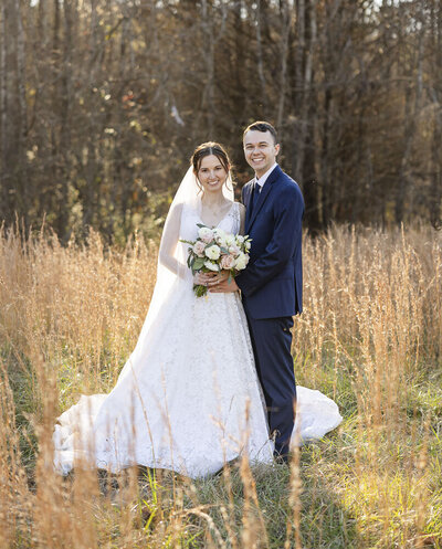 bride and groom smiling while standing in a field