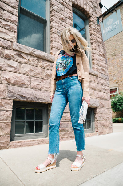 Sarah Klongerbo wearing sunglasses, jeans, and a graphic tee holding a newspaper and walking down the street