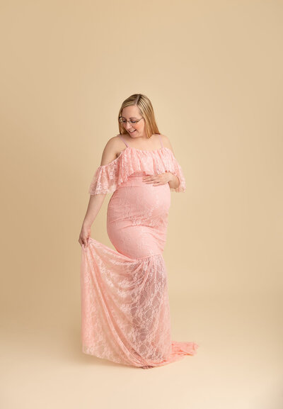 pregnant mom wearing pink dress in studio by philadelphia maternity photographer