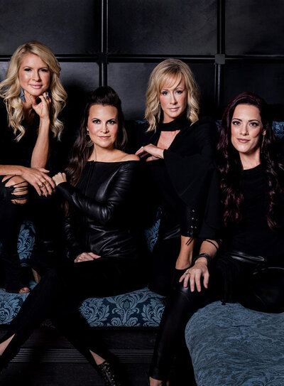 Band portrait of female music group The Mrs seated against black background all wearing black shirts
