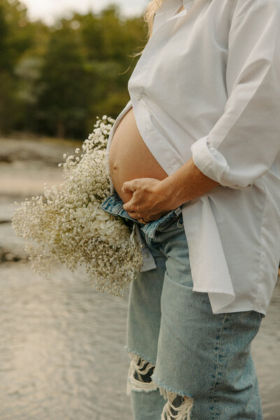 Woman posing with flowers at the creek at The Mill At Fine Creek for her maternity photos