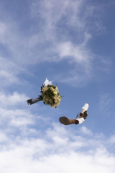 Bride tossing her bouquet into the air beneath a clear blue sky during a Utah wedding, captured by Lamblight Photography