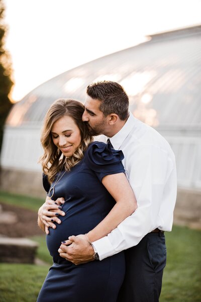 A couple expecting a baby share an affectionate moment outdoors, captured by a talented Pittsburgh PA photographer.