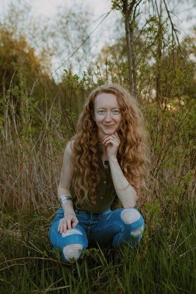 Kvinna med rött hår bland grönska.