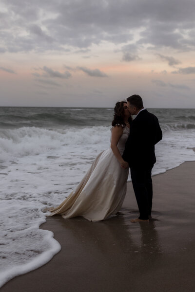 bride-and-groom-hugging-eachother-at-the-beach-during-sunset