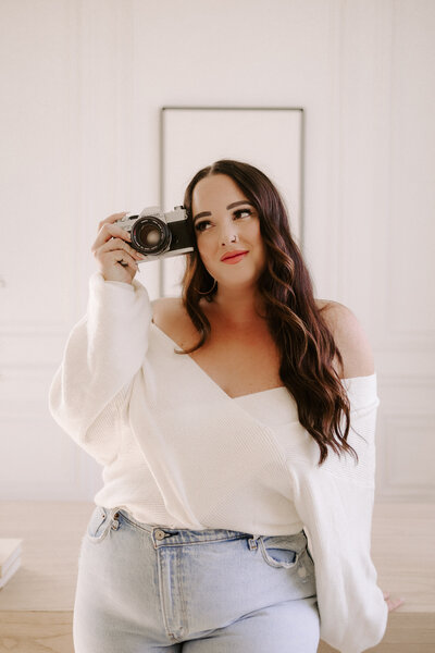 Sharlie Faye, self portrait holding a 35mm camera.  Wearing blue jeans and a white top