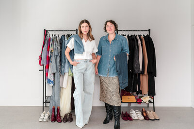 Two wardrobe stylists in stylish denim outfits standing in front of clothing racks for modern business portrait