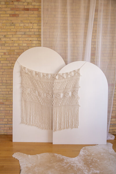 Macrame decor hanging on two white wooden arch backdrops.