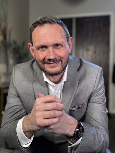 Confident middle-aged man in a light gray suit smiling warmly, representing a professional Peace Coach offering spiritual and practical guidance. Ideal for personal growth, emotional resilience, and finding personal peace