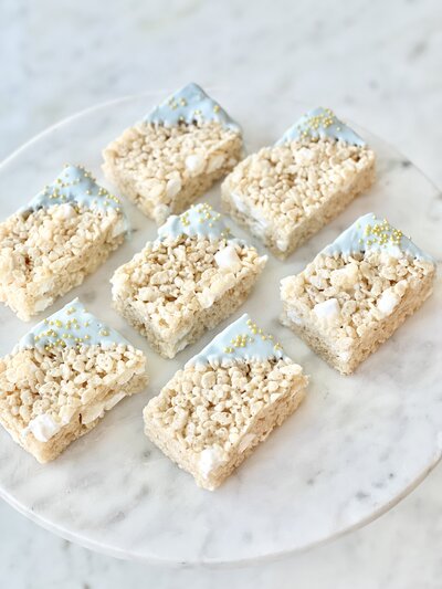 Diagonal white chocolate dipped rice krispie treats in blue with gold sprinkles