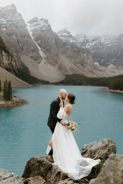 A bride and groom share a kiss over looking Maligne Lake in Banff, AB.