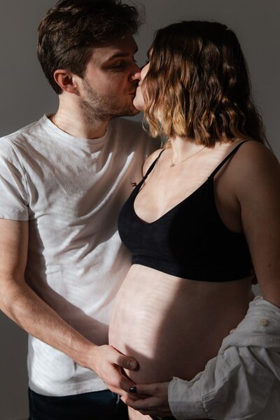 un couple de futurs parents qui s'embrassent au soleil pendant une séance photo grossesse en studio à la tour du pin par studio sensigraphie photographe grossesse bourgoin jallieu
