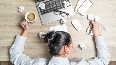 Woman lays on her desk, stressed out with lots of papers around her.