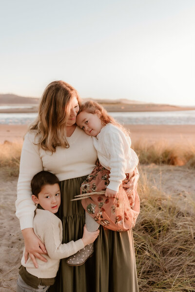 Hope holding her two children at the beach in the sunset.