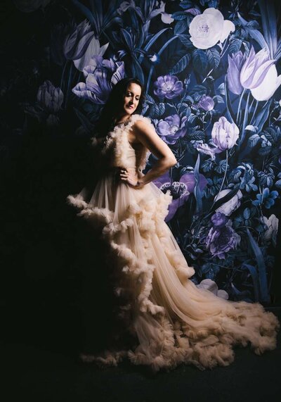 Portrait of woman standing in front of floral back drop wearing couture gown