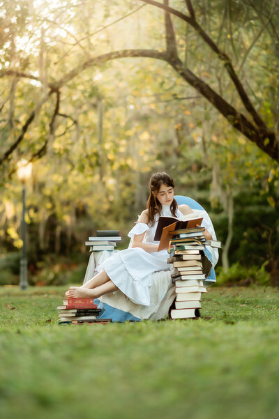 high school senior girl sitting in a chair surrounded by books in a beautiful park in Winter Park, FL during her senior photo session. 
