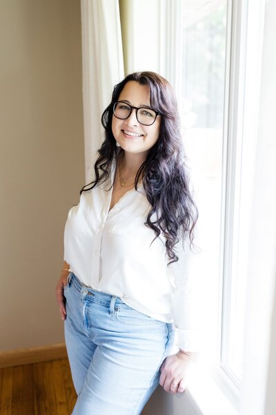 Aubre wearing a white button down shirt standing in front of a sun drenched window