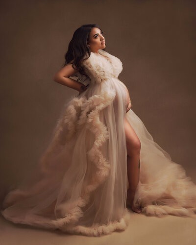 Maternity mother posed in a tan couture gown standing on brown backdrop near seattle