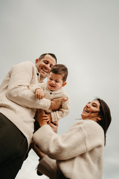 Family of five standing together on a lakeside rock during an outdoor photo session in Stanhope, NJ, with autumn trees and hills in the background, captured by Burkat Photography