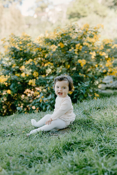 Baby girl sitting on grass and smiling.