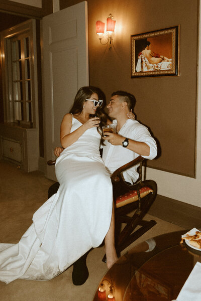 bride sitting on groom's lap sharing a toast