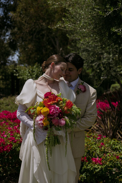 Yered hugging his bride, Regan, from behind while she rests her head on his, holding her spring bouquet.