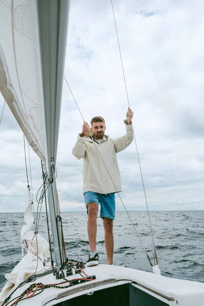 Segler steht am Bug einer Segelyacht, hält sich an den Wanten fest und schaut Richtung Cockpit