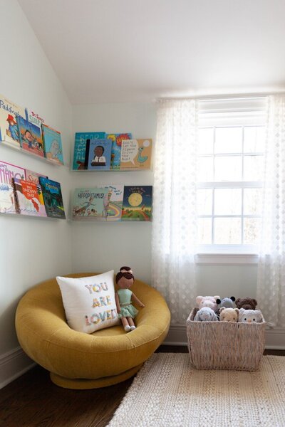 A stylish and cozy reading nook featuring acrylic book shelves, a West Elm  Petite Groovy Swivel Chair in Dark Horseradish, and Target Pillowfort stuffed animals.